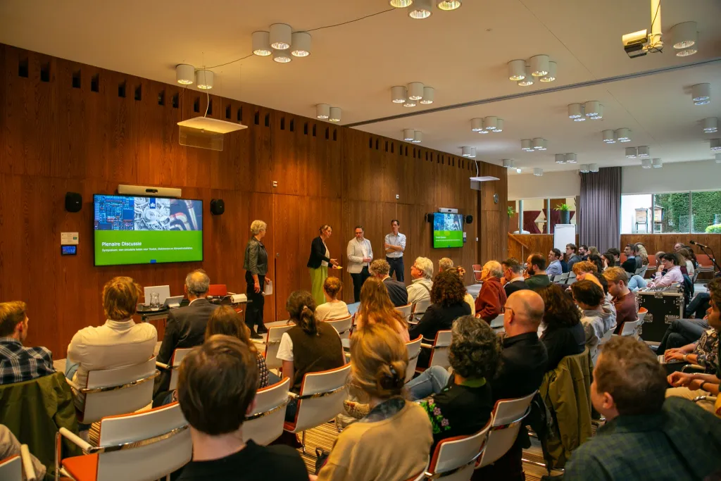 Seminarzaal met een discussie tussen publiek en een viertal mensen voor het publiek