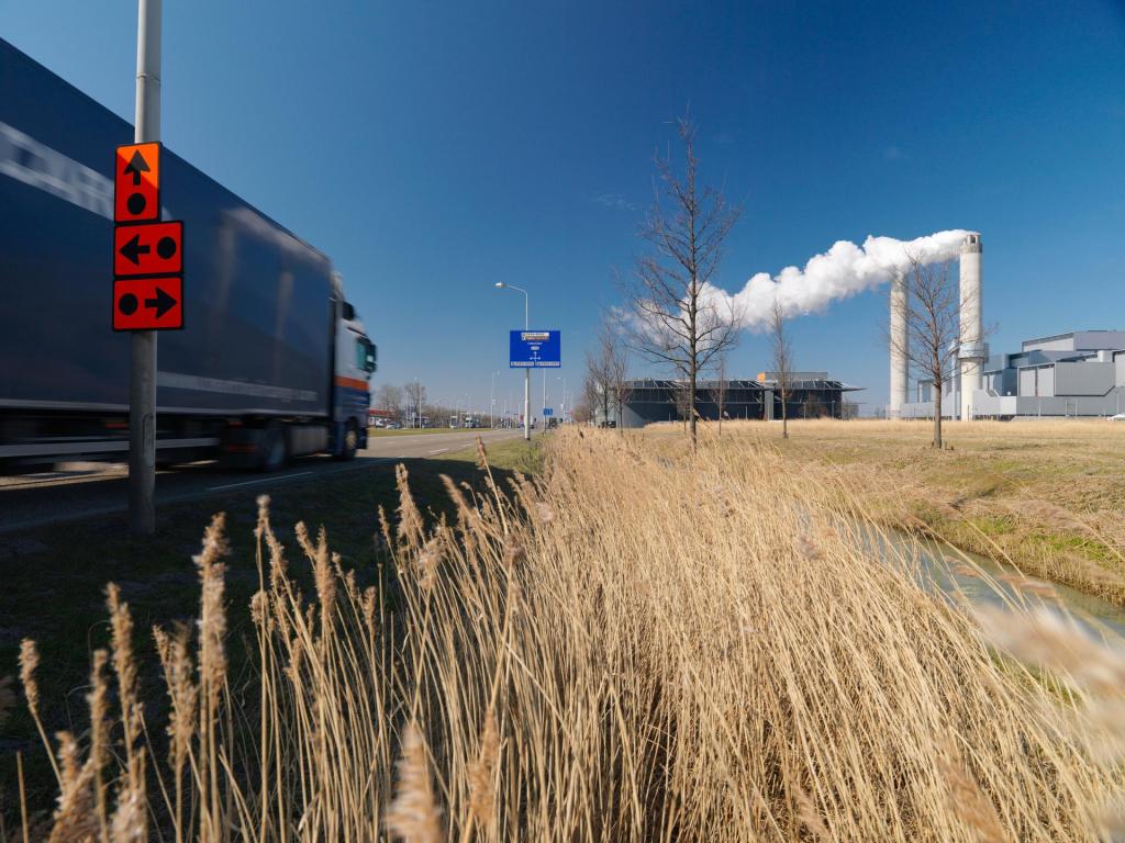 Foto van vrachtwagen rijdend door industriegebied met rokende schoorstenen op de achtergrond